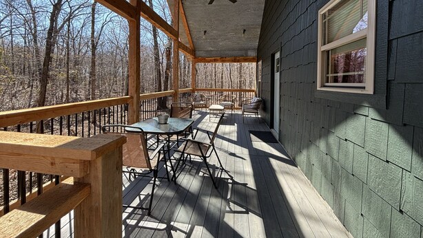 Um deck coberto com mesa e cadeiras, um ventilador de teto e uma janela com vista para uma floresta.