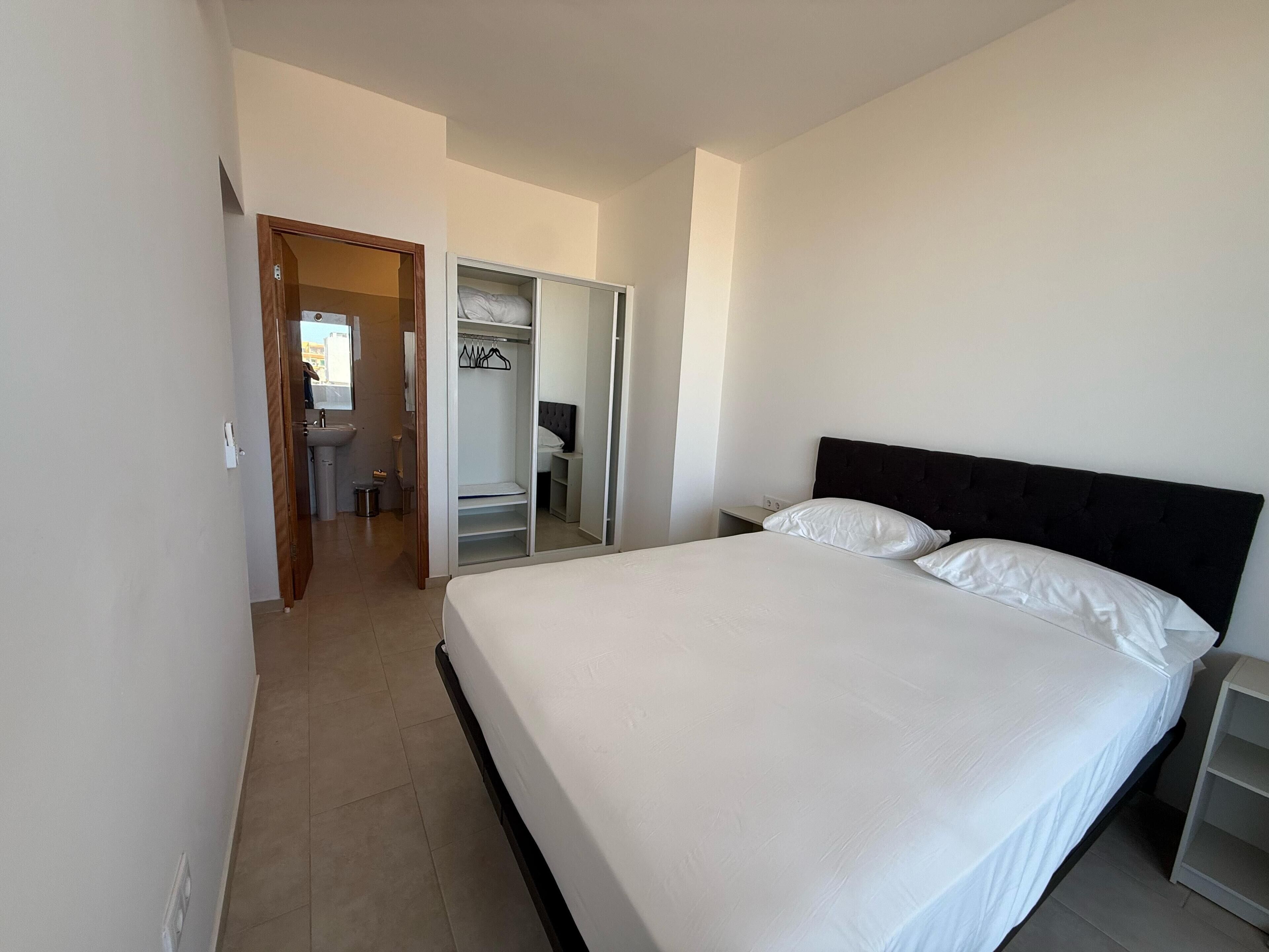 Un dormitorio con una cama grande, un armario y un baño visible a través de una puerta abierta.