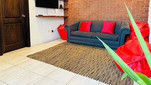 A living room with a dark grey sofa, red cushions, a flat-screen TV mounted on a white wall, and a brick wall. - Casa Quetzal Xela, ideal house for a comfortable stay and central location. (Quetzaltenango)