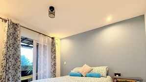 A bedroom with a bed, curtains, a nightstand, and a view of the outdoors. - Casa Quetzal Xela, ideal house for a comfortable stay and central location. (Quetzaltenango)
