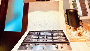 A kitchen with a gas stove, wooden beams, a stainless steel range hood, and a window with a view. - Casa Quetzal Xela, ideal house for a comfortable stay and central location. (Quetzaltenango)