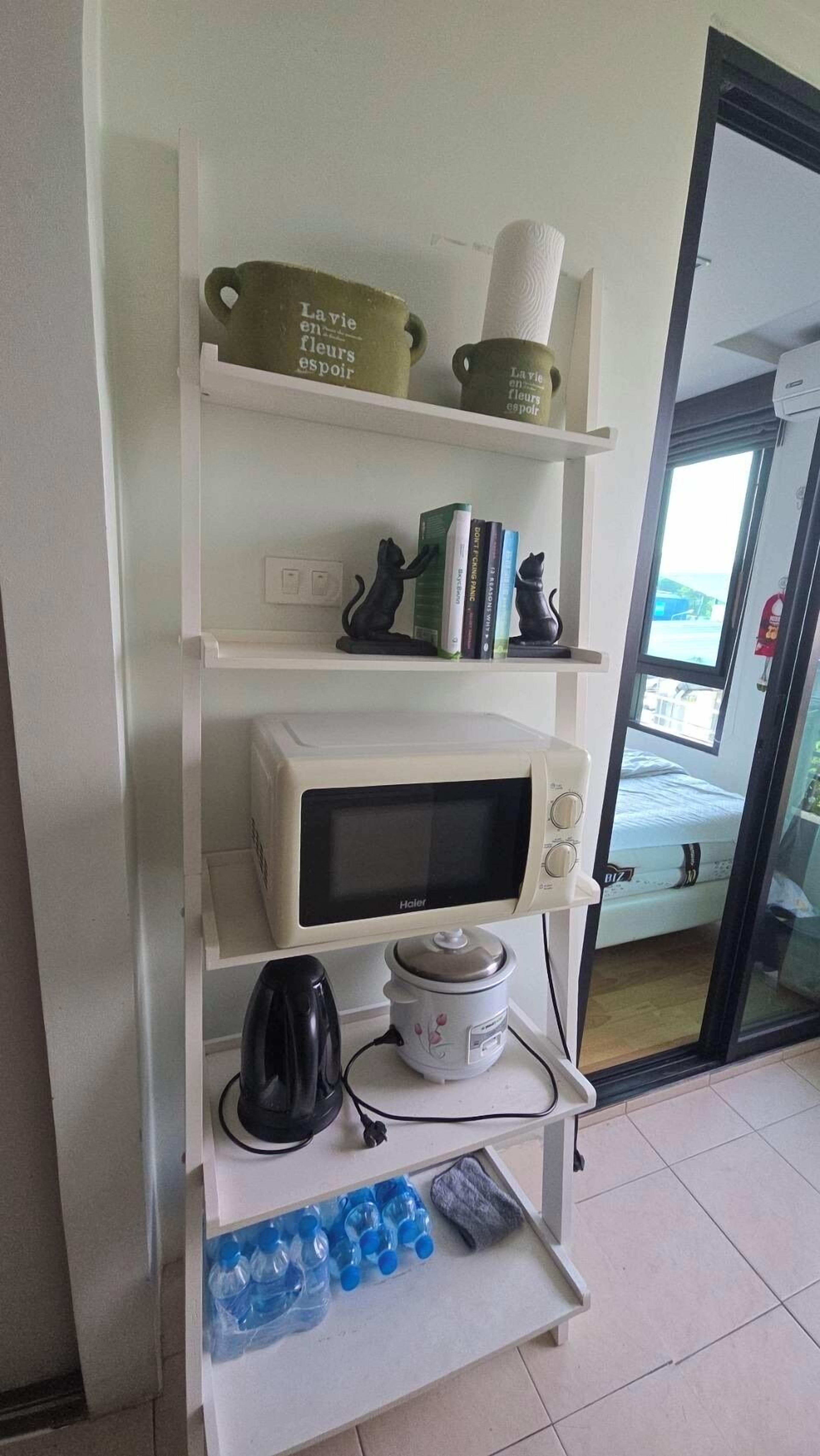 A kitchenette with a microwave, kettle, and water bottles on a shelf.