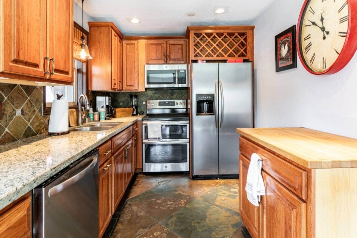 A kitchen with wooden cabinets, stainless steel appliances, a granite countertop, and a clock on the wall.