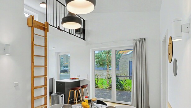 A dining area with a round table set for four, a wooden ladder, and a view of the outside. - Windlicht 244 by Interhome (Lembruch)