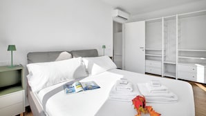 A modern hotel room with a neatly made bed, a bedside table with a lamp, a wardrobe, and a view of the city. - Ulivo Bike & River Apartment, Arco, Italy (Arco)