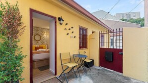 A small, yellow building with a red door, a bed with white bedding, a small table with chairs, and a potted plant. - GuestReady - Porto's relaxing nook (Porto)