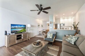 Una sala de estar moderna con televisión de pantalla plana, ventilador de techo, comedor y cocina.