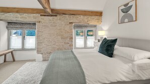 Ein Schlafzimmer mit Steinsturz, Holzbalken, einem Bett mit weißen Leinen, einer grünen Decke und Blick durch ein Fenster.