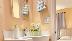 A bathroom with a white sink, a mirror, a towel rack, a toilet paper holder, and a door leading to a bedroom. - Serene cottage with AC in Milpitas - 2 bedrooms available (Milpitas)