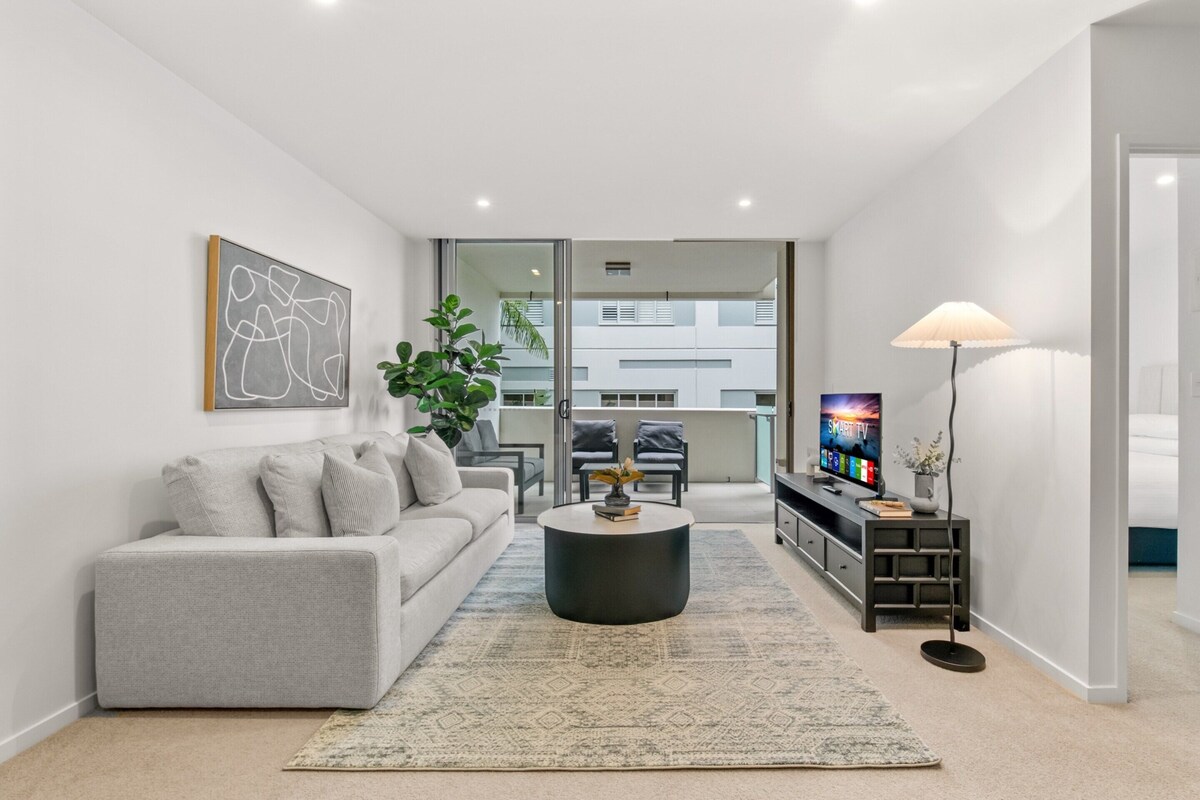 Una sala de estar moderna con un sofá gris, una mesa de centro redonda, un televisor y una planta.