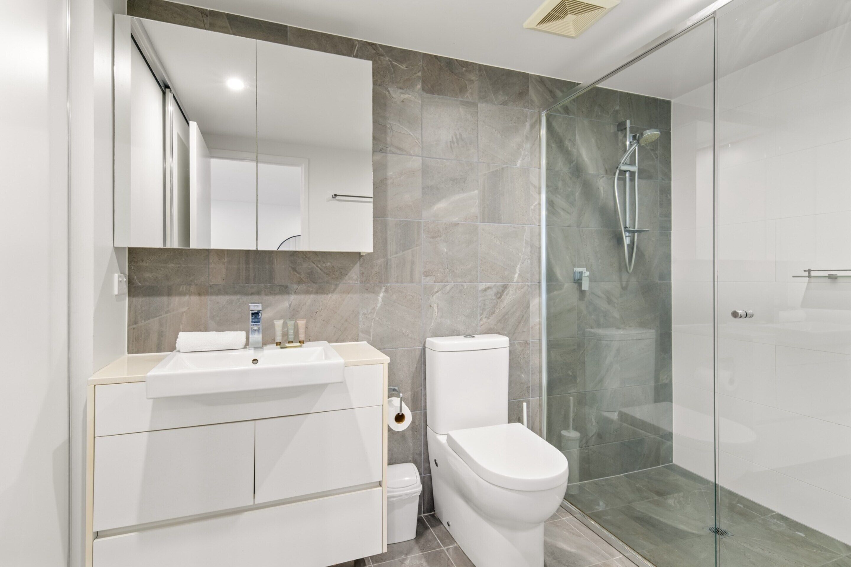 A modern bathroom with a glass-enclosed shower, a white sink, and a toilet.