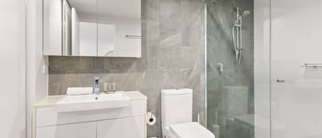A modern bathroom with a glass-enclosed shower, a white sink, and a toilet.