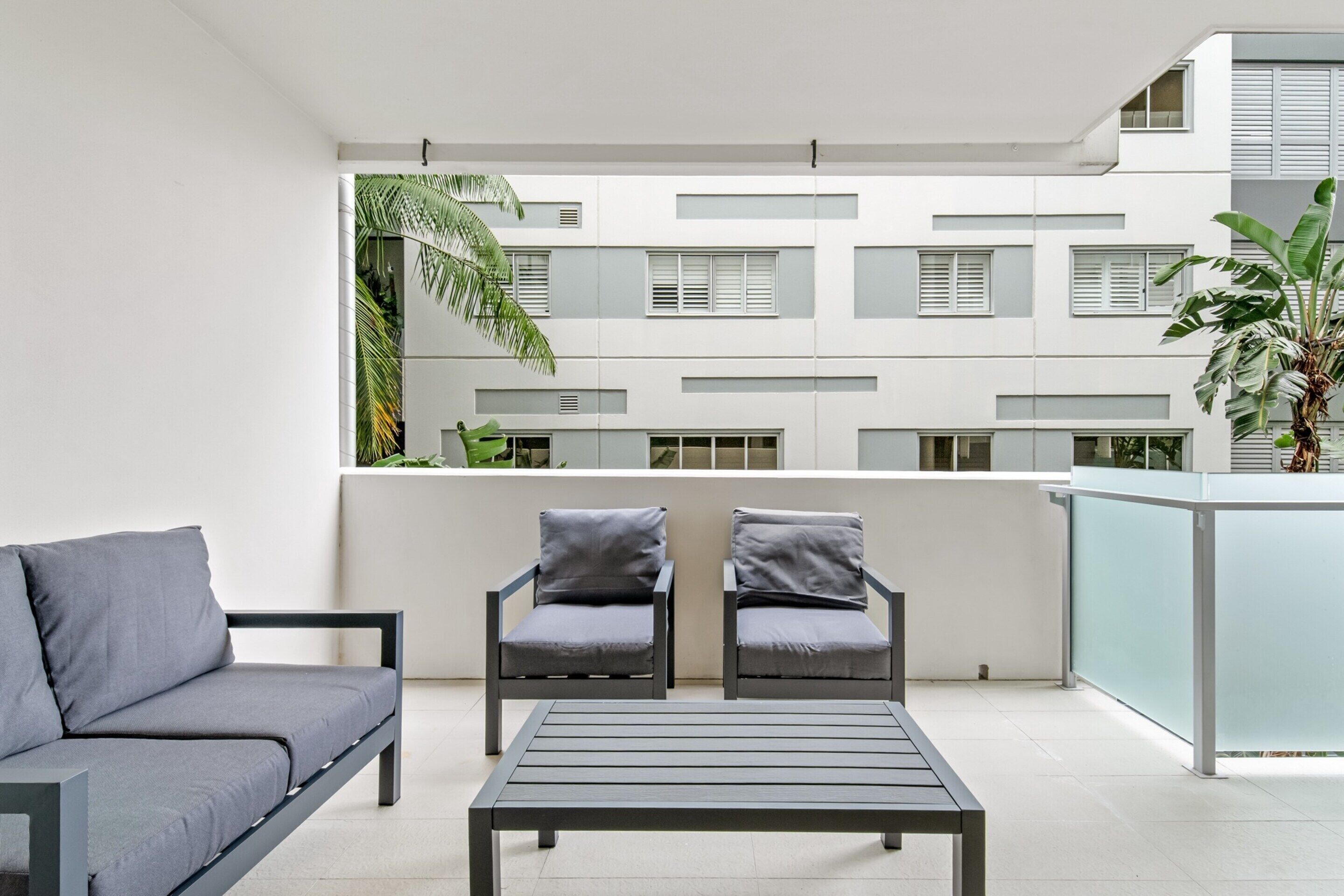 A modern balcony with a grey sofa, two armchairs, and a table.