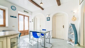 Een eetruimte met een glazen tafel en blauwe stoelen, een houten kast en een witte deur met een klein plankje.