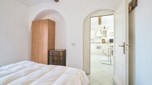 Een slaapkamer met een bed, een houten garderobe en een deur naar een keuken.