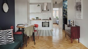 Een moderne keuken met witte kasten, een eethoek met tafel en stoelen, en een gang naar een woonkamer.