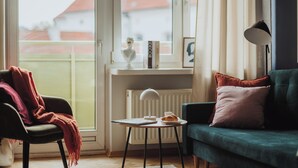 Een gezellige woonkamer met een groene bank, een zwarte fauteuil en een kleine tafel met een boek en een kop.