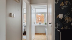 Een hal met een houten vloer, een raam met herfstbladeren en een deur met lichtschakelaar.