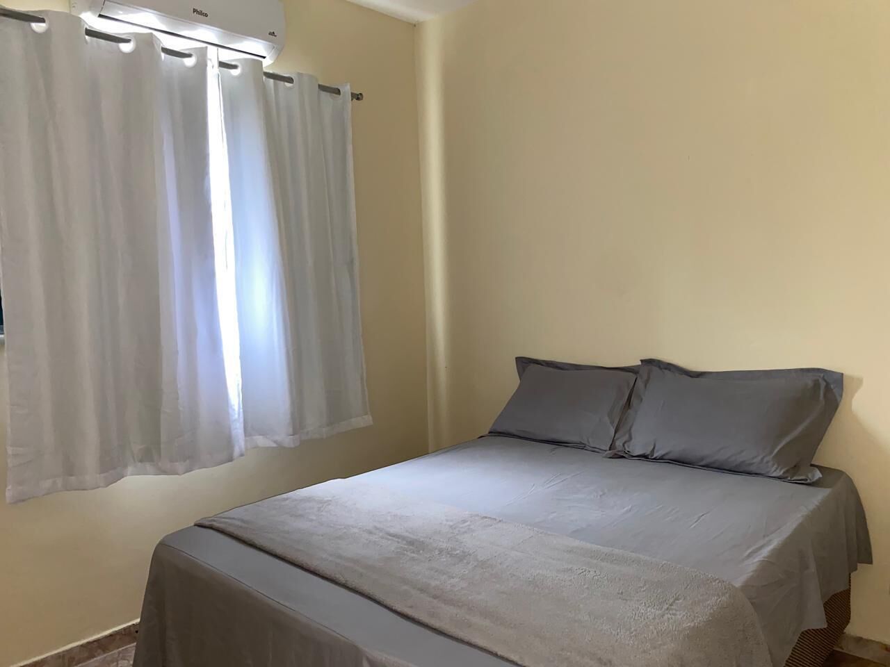 Ein Schlafzimmer mit einem Bett, zwei Kissen und einem Fenster mit Vorhängen.