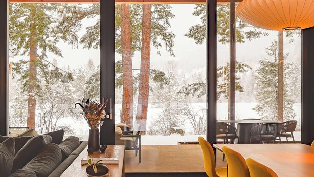 A modern interior with a sofa, dining table, chairs, and a view of snow-covered trees through large windows. - Ursa Minor – Spacious 4BR Retreat near Mazama (Winthrop)