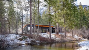 A modern cabin with large windows, surrounded by a forest and a river. - Ursa Minor – Spacious 4BR Retreat near Mazama (Winthrop)