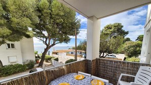 Un balcon avec une table ronde prévue pour quatre personnes, des chaises en plastique blanches et une vue sur la mer et les bâtiments.