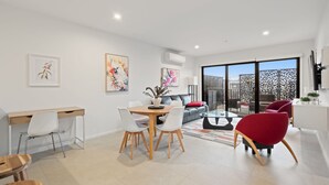 A modern living room with a dining area, a sofa, and a red chair. There is a desk with a chair, a coffee table, and artwork on the walls. - Stylish 2-bed Townhouse With Balcony (Canberra)