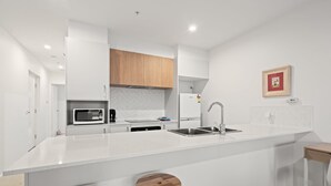 A modern kitchen with white cabinetry, a large island with stools, a built-in microwave, and a stainless steel sink. - Stylish 2-bed Townhouse With Balcony (Canberra)