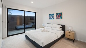 A bedroom with a bed, a nightstand, and a sliding glass door leading to a balcony. - Stylish 2-bed Townhouse With Balcony (Canberra)
