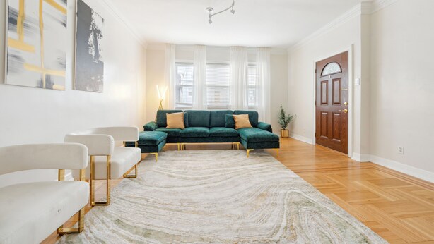 A living room with a sectional sofa, a white armchair, a patterned rug, and a wooden floor. - Spacious 3BR Luxe Escape near NYC (Yonkers)