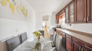 A modern kitchen with wooden cabinets, a stainless steel microwave, and a glass dining table with chairs. - Spacious 3BR Luxe Escape near NYC (Yonkers)