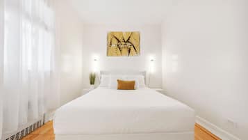 A bedroom with a large bed, white bedding, a single decorative pillow, a wall-mounted abstract painting, and two bedside lamps.