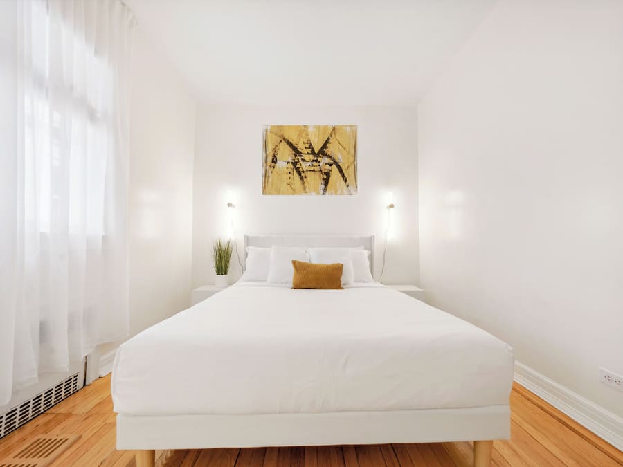 A bedroom with a large bed, white bedding, a single decorative pillow, a wall-mounted abstract painting, and two bedside lamps.
