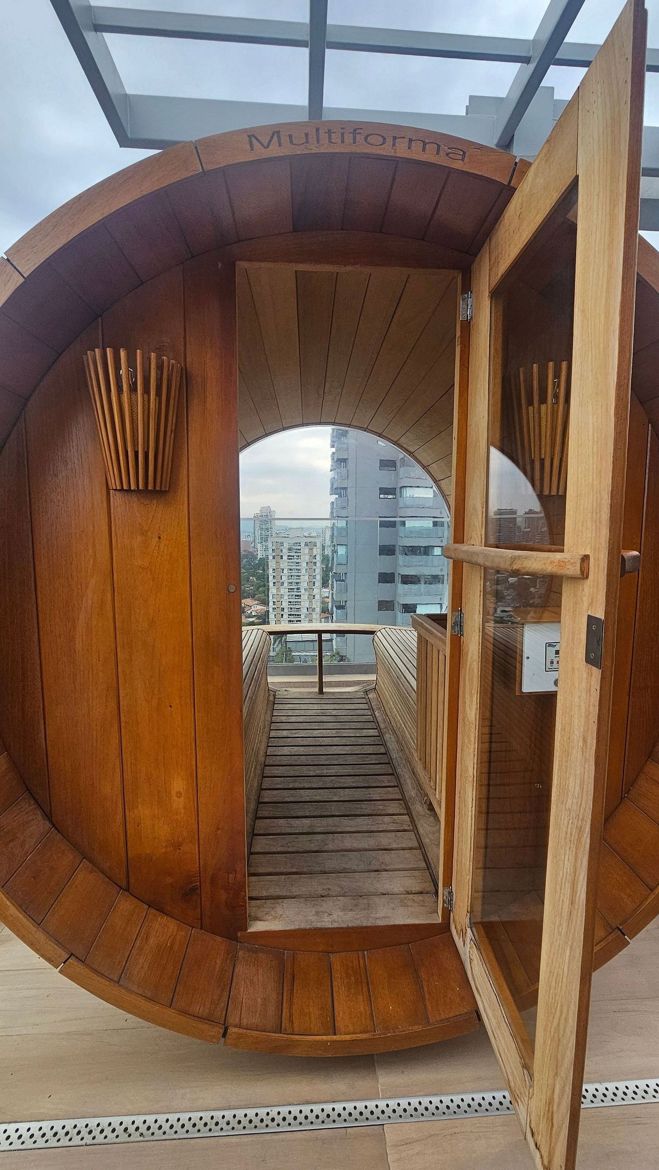 A wooden, circular structure with a glass door, leading to a balcony with a view of buildings.