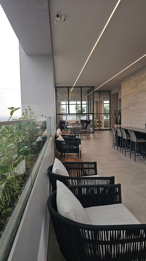 A modern outdoor seating area with black wicker furniture and a glass railing overlooking a cityscape. - Terrae Pinheiros (São Paulo)