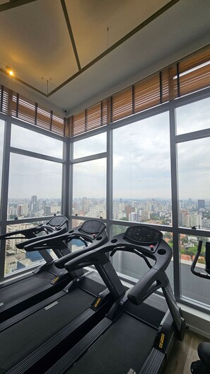 Un gimnasio con cintas de correr y equipo de ejercicio, ventanas amplias con vista a la ciudad.