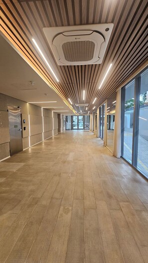 A spacious corridor with wooden flooring, large windows, and a ceiling with a central ventilation unit. - Terrae Pinheiros (São Paulo)