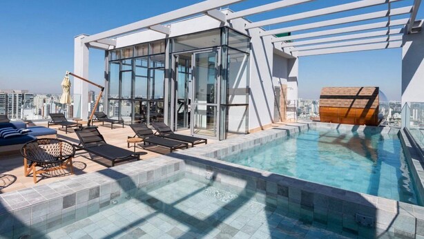 A rooftop pool area with lounge chairs, a glass-enclosed structure, and a view of the city skyline. - Terrae Pinheiros (São Paulo)