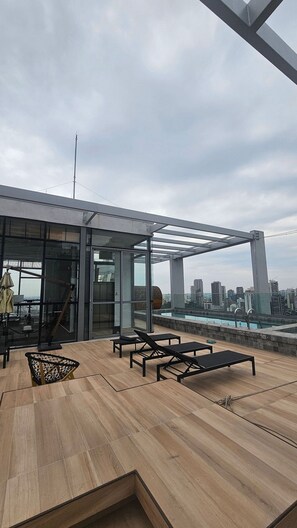 Una terraza en la azotea con piscina, sillas de descanso y un área acristalada con vistas al horizonte de la ciudad.