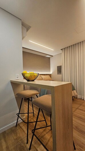 A modern kitchenette with a wooden countertop, two bar stools, a yellow bowl, and a built-in oven. - Terrae Pinheiros (São Paulo)