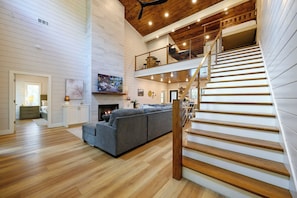 Un vaste espace de vie comprenant un grand canapé gris, un plancher en bois, une cheminée et un escalier avec une rampe en bois.