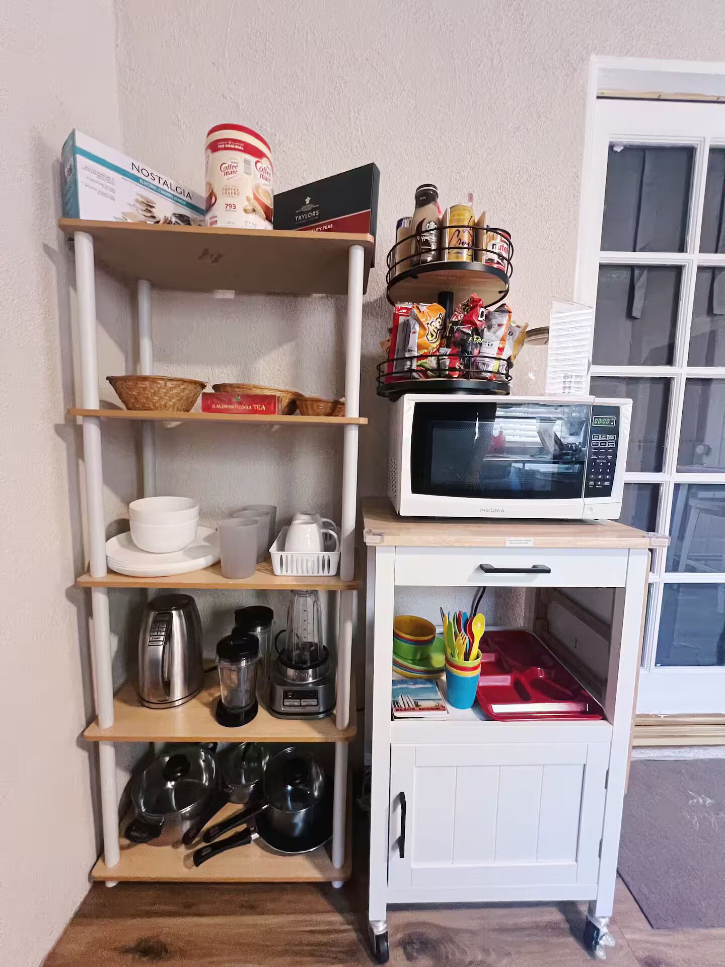 Een keukenhoek met planken vol keukengerei, een magnetron en een kast met bestek.