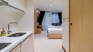 A hotel room with a modern design, including a white sink, a bed with a wooden frame, and a large window with curtains. - Ocean Breeze1BR Steps from the Sea C244 (Rawai)