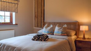 A bedroom with a wooden headboard, a bed with white bedding, a bedside table with a lamp, and a window with patterned curtains. - 3 bedroom accommodation in Kingsthorpe, near Northampton (Kingsthorpe, near Northampton)