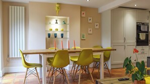 A dining area with a wooden table, yellow chairs, and a shelf with decorative items. - 3 bedroom accommodation in Kingsthorpe, near Northampton (Kingsthorpe, near Northampton)
