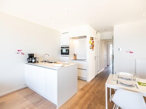 A modern kitchen with a central island, a dining area with a table set for two, and a hallway leading to bedrooms.