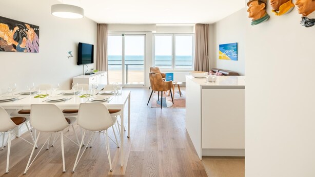 Een moderne hotelkamer met een zithoek, een keuken, een televisie en een balkon met uitzicht op zee.