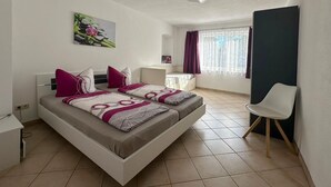 Ein modernes Schlafzimmer mit einem Bett, Nachttischen, einem Sessel und einem Fenster mit Vorhängen.
