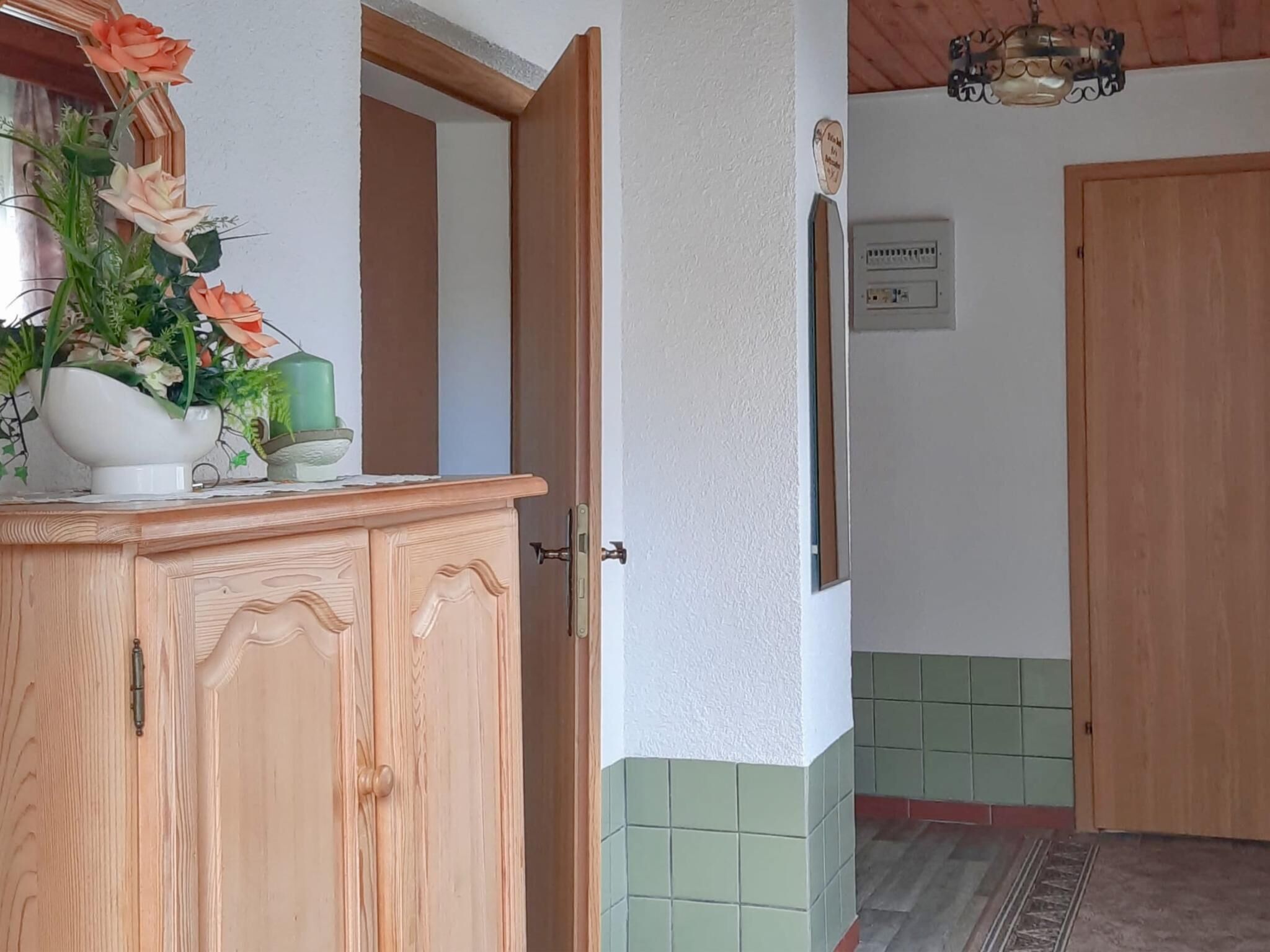 A wooden cabinet with a mirror, a vase of flowers, and a green candle.