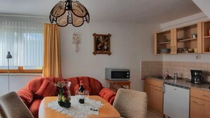 Een gezellige woonkamer met een bank, een eettafel met stoelen, een televisie en een keuken met kasten en apparatuur.